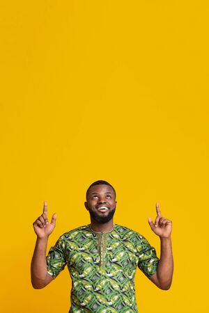 Joyful african american guy looking and pointing at empty space, yellow backgroundの写真素材