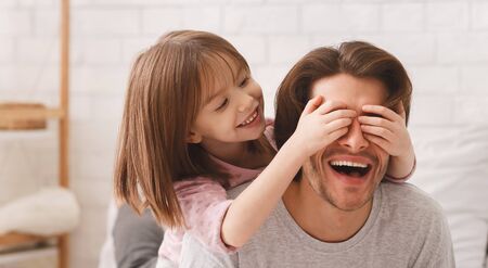 Little Playful Girl Covering Her Father Eyes With Palms, excited dad is laughing, panorama with copy...