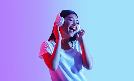 Favorite music online. Asian girl in modern headphones sings with eyes closed, free space, studio...
