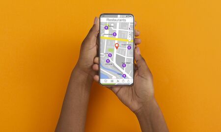 African American girl holding cellphone with map and restaurant navigation pointers on screen,...