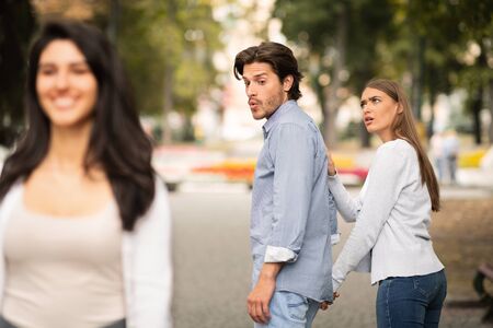 Jealousy. Jealous Girlfriend Calling Boyfriend Distracted By Other Attractive Woman Walking During...