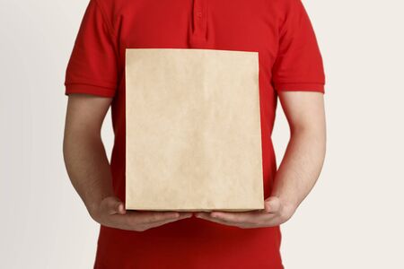 Neat delivery. Courier in red uniform holds paper package in his hands, close up, free space, croppedの写真素材