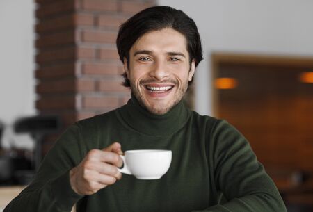 Portrait of young cheerful man drinking tea or coffee at cafe aloneの写真素材