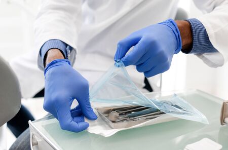 Black dentist hands opening sealed set of sterile dental tools, close up