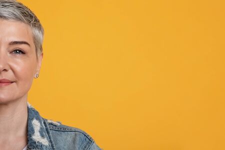Half-face portrait of beautiful middle-aged woman with soft skin over yellow studio background with...