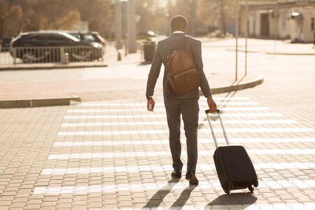 Unrecognizable African American Businessman Crossing Road Walking With Suitcase In City. Copy Space, Back View.の写真素材