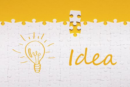 Great idea. Last detail for assembled white puzzle with inscription and lit lamp on yellow backgroundの写真素材