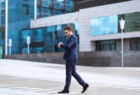 Serious business owner walking and looking at his watch in city centerの写真素材
