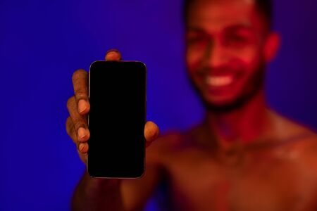 Workout App. Muscular African Guy Showing Phone Empty Screen Recommending Fitness Application Over Blue Studio Background. Mockup, Selective Focusの写真素材