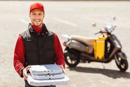 Smiling Courier Man Offering Pizza Boxes To Camera Posing Standing Near Motorbike Outside. Food Delivery. Free Spaceの写真素材