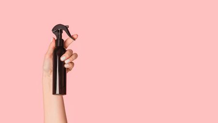 Cropped view of girl hand showing black spray bottle with cosmetic product on pink background, copy space. Panoramaの写真素材