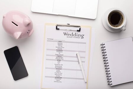 Wedding budget planning concept. Pink piggy bank, checklist what to buy, notebook and cellphone with black blank screenの写真素材