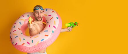 Expressive guy in inflatable ring shoots water guns with open mouth