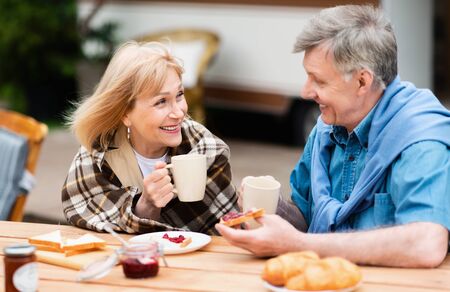Affectionale elderly couple having coffee with toasts and jam for lunch in countryside during vacationの写真素材