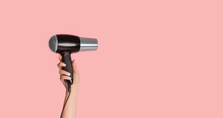 Closeup view of female hand showing modern hairdryer on pink background, empty space. Panoramaの写真素材