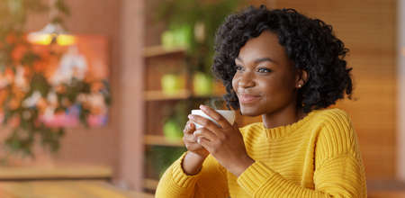 Time for coffee. Romantic black girl sitting at cafe alone, enjoying cup of coffee at cafe, panorama...