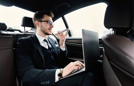 Voice Recognition, Search Technology Concept. Worker in glasses using smart phone and pc sitting in carの写真素材