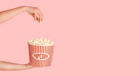 Cropped view of young girl holding jumbo bucket of popcorn on pink background, free space. Panoramaの写真素材