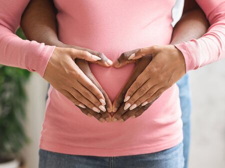 Love, family, pregnancy concept. Hands of african wife and husband on pregnant woman belly, closeupの写真素材