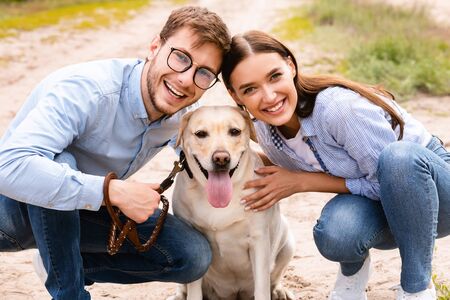 Portrait of happy young couple hugging their lovely dog and smiling at camera, walking outdoorsの写真素材
