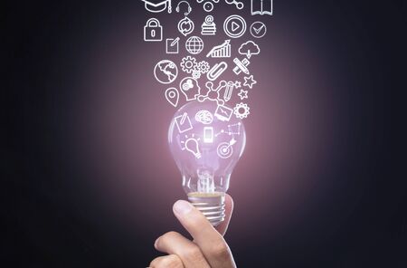 Qualification concept. Hand holds luminous bulb, symbols knowledge, graphics, settings and lock flow up from it, double exposure with futuristic symbolsの写真素材
