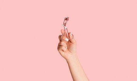 Closeup of beautician hand holding eyelash curler on pink background, panorama