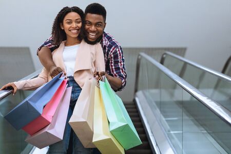 Sales Season. Joyful African Couple With Lots Of Shopping Bags In Hands Riding Escalator In Mall, Copy Spaceの写真素材