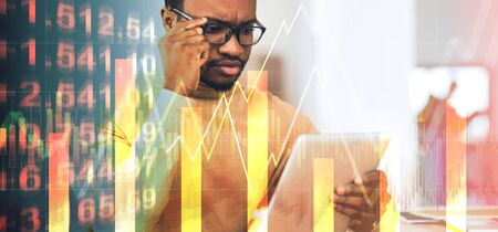 Serious African american businessman working with tablet computer at office, collage with economic info on imaginary screen, copy space. Panoramaの写真素材