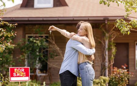 Millennial couple with key embracing in front of their new house outside, free spaceの写真素材