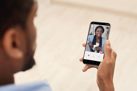 Back view over the shoulder of black guy using online dating app or website, looking at female...