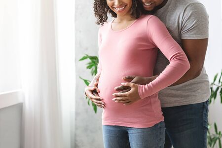 Cropped of african couple waiting for baby hugging at home next to window, family concept
