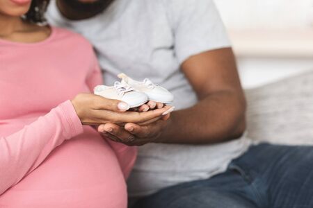 Closeup of small baby footwear in black man and woman hands, home interior, copy spaceの写真素材