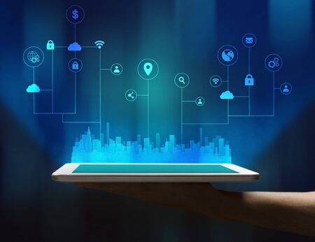 Hand Holding Digital Tablet With Hologram Of Urban City Buildings On Blue Background. Internet Of...