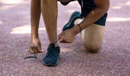 Young sportsman tying shoelaces during his morning run outdoors, closeup of legs. Panoramaの写真素材