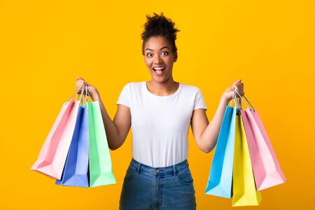 Big Sale Concept. Happy african girl holding shopping bags in both hands isolated over yellow studio wallの写真素材