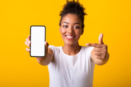 Choose This. Black woman presenting cell phone with white blank screen for mockup, orange wall, empty spaceの写真素材