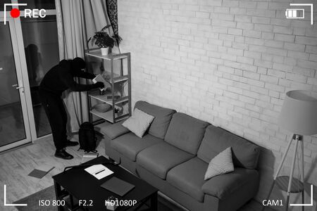 Top view of stealthy disguised criminal searching cash or important papers, holding book, black and...
