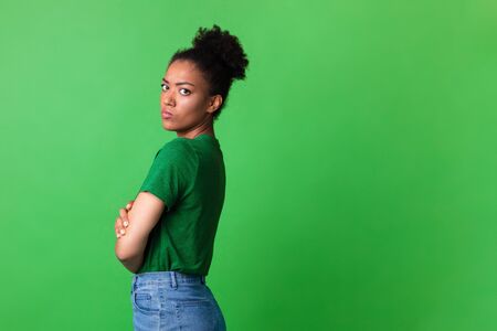 Feeling Offended. Half-turned sad black girl with crossed arms and pursed lips looking at camera over green studio wallの写真素材