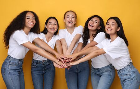 Five Diverse Girls Holding Hands Smiling To Camera Posing On Yellow Studio Background. Female Unity...