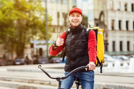 Food Delivery Service. Courier Gesturing Thumbs Up Standing With Delivering Backpack And Bike In City Outdoor. Free Spaceの写真素材