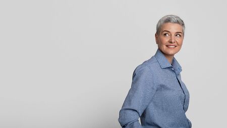 Elegant Smiling Middle Aged Woman Looking At Copy Space, Standing Half-Turned Over Light Background,...