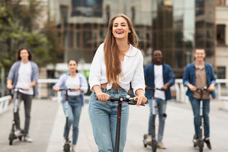 Youth Concept. Young beautiful girl riding an electric scooter in the summer on the street, having fun with friendsの写真素材