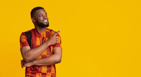 Happy african american man in bright traditional costume pointing at free space, panoramaの写真素材