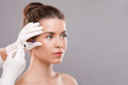 Cosmetology concept. Young woman getting facial beauty injection for eye wrinkles, empty spaceの写真素材
