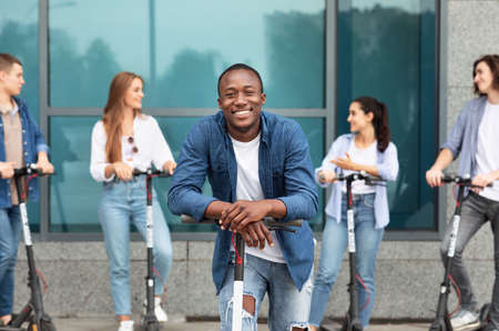 Youth Concept. African american guy leaning on e-scooter, looking at camera, spending time with friendsの写真素材