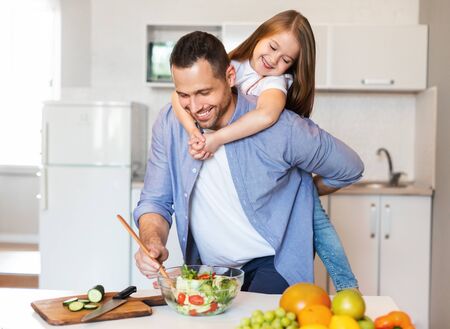 Happy Fatherhood. Dad Cooking Holding Little Daughter On Shoulders Enjoying Time Together In Kitchen At Home.の写真素材