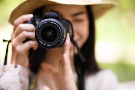 Young asian girl taking photos in the park with modern camera. Closeup shot with selective focus on lensの写真素材