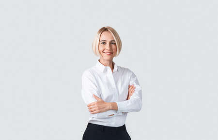 Beautiful businesswoman in formalwear standing with crossed arms on light studio backgroundの写真素材