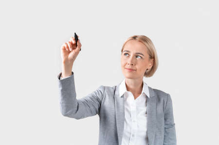 Attractive business lady writing or drawing on virtual screen against light background, space for your designの写真素材