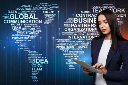 Young businesswoman using tablet computer, collage with world map made of economy related words,...